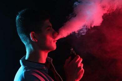 Photo of Man using electronic smoking device in neon lights on black background