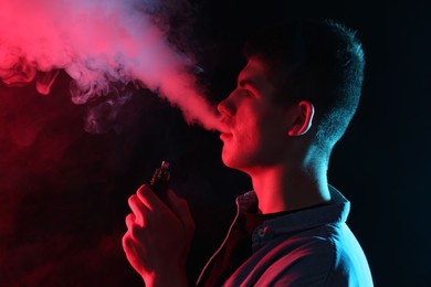 Photo of Man using electronic smoking device in neon lights on black background