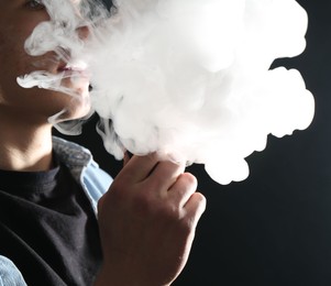 Photo of Man using electronic smoking device on black background, closeup