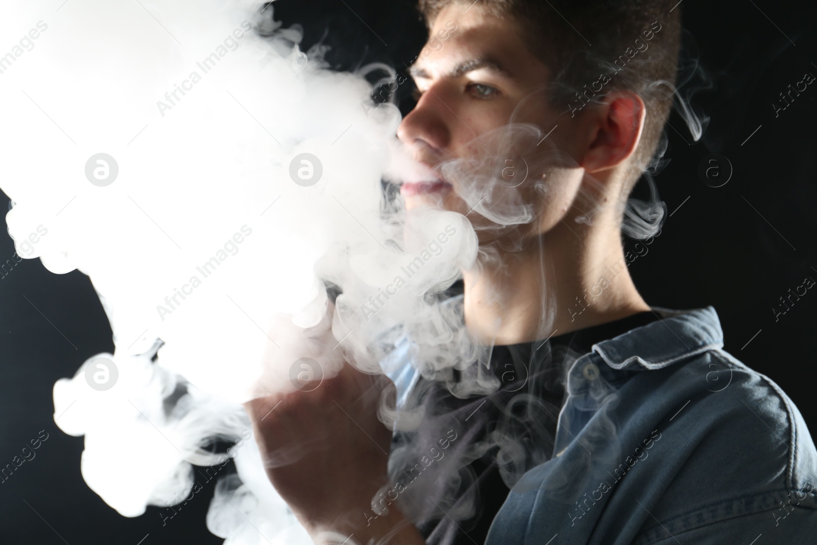 Man using electronic smoking device on black background Photo of Man using electronic smoking device on black background