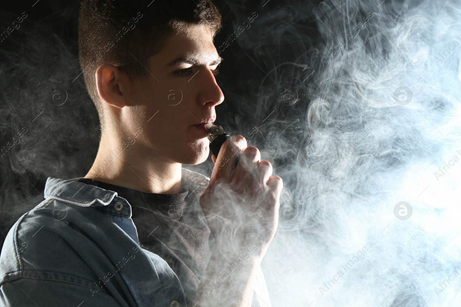 Man using electronic smoking device on black background Photo of Man using electronic smoking device on black background