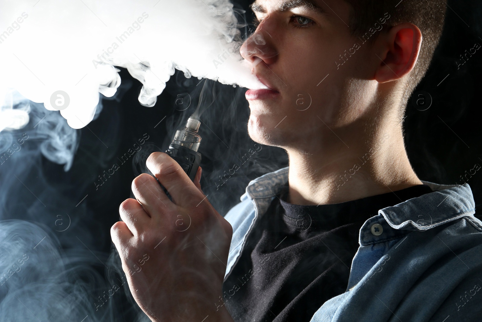 Man using electronic smoking device on black background Photo of Man using electronic smoking device on black background