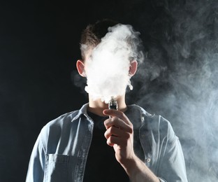 Photo of Man using electronic smoking device on black background