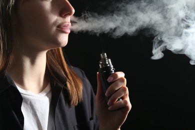 Photo of Woman using electronic smoking device on black background, closeup