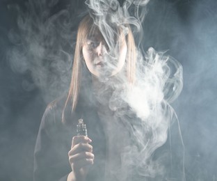 Photo of Woman using electronic smoking device on dark background