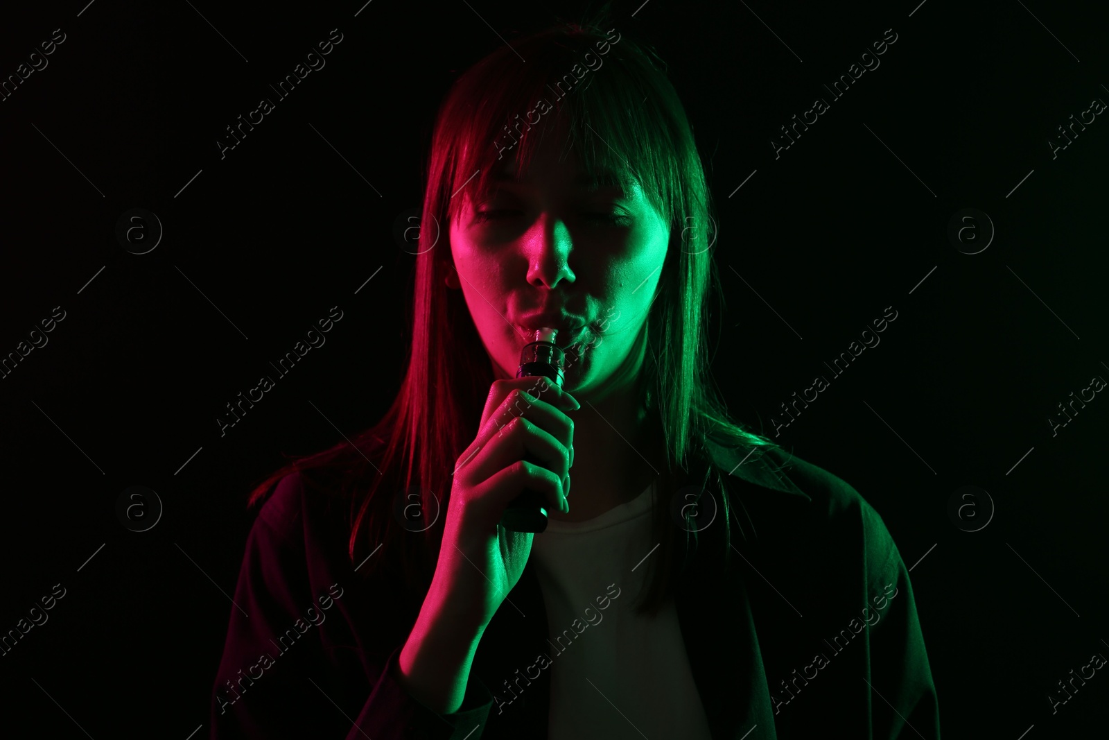 Woman using electronic smoking device in neon lights on black background Photo of Woman using electronic smoking device in neon lights on black background