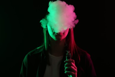 Photo of Woman using electronic smoking device in neon lights on black background