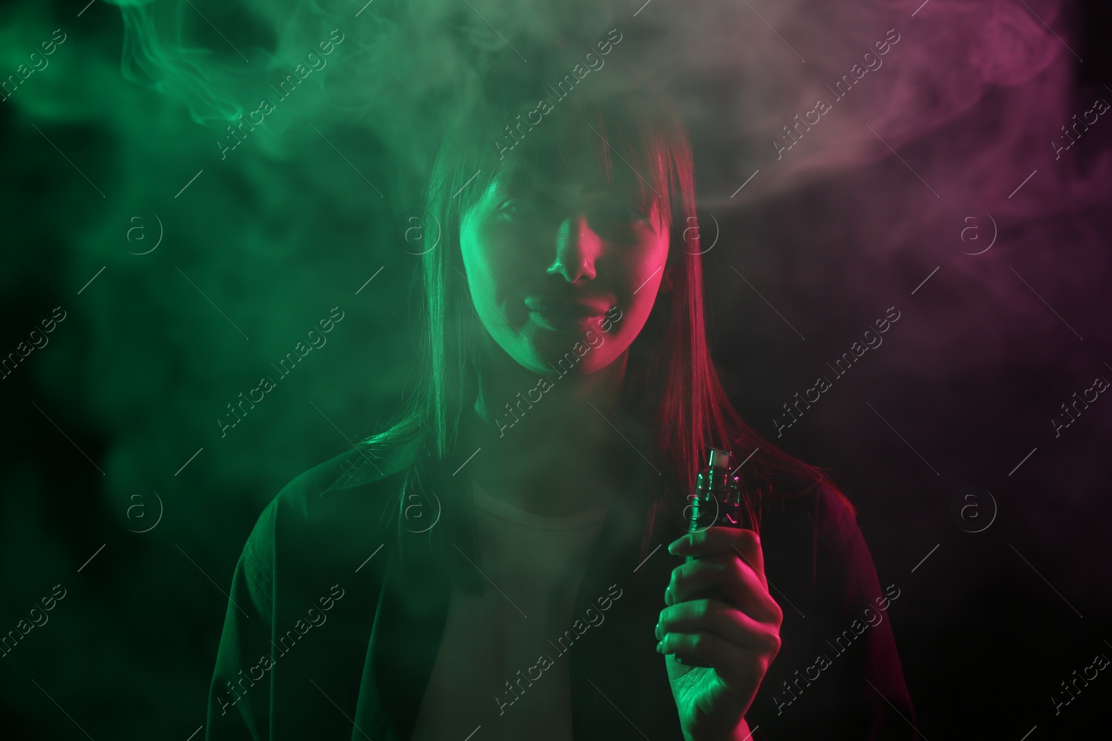 Woman using electronic smoking device in neon lights on black background Photo of Woman using electronic smoking device in neon lights on black background