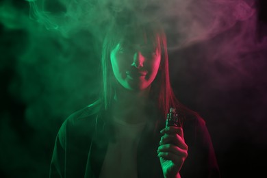 Photo of Woman using electronic smoking device in neon lights on black background