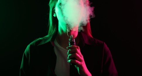 Photo of Woman using electronic smoking device in neon lights on black background