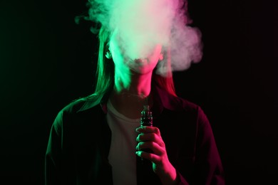 Photo of Woman using electronic smoking device in neon lights on black background