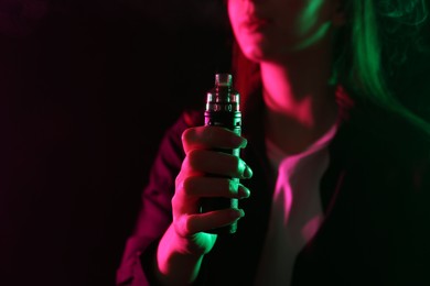 Photo of Woman using electronic smoking device in neon lights on black background, closeup. Space for text