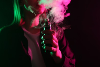 Photo of Woman using electronic smoking device in neon lights on black background, closeup. Space for text
