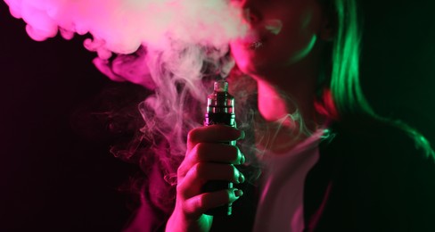 Photo of Woman using electronic smoking device in neon lights on black background, closeup. Space for text
