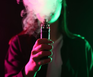 Photo of Woman using electronic smoking device in neon lights on black background, closeup