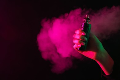 Photo of Woman using electronic smoking device in neon lights on black background, closeup. Space for text