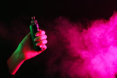Photo of Woman using electronic smoking device in neon lights on black background, closeup. Space for text