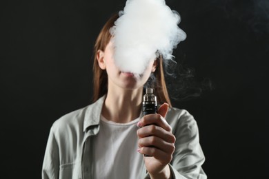 Photo of Woman using electronic smoking device on black background
