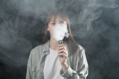 Photo of Woman using electronic smoking device on dark background
