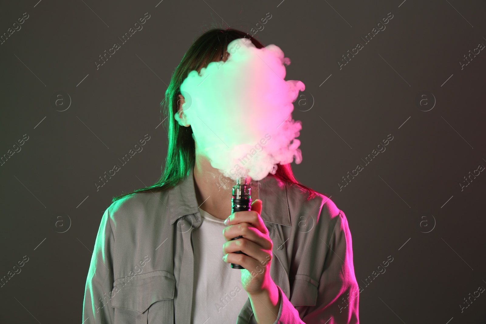 Woman using electronic smoking device in neon lights on grey background Photo of Woman using electronic smoking device in neon lights on grey background