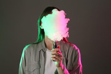 Photo of Woman using electronic smoking device in neon lights on grey background