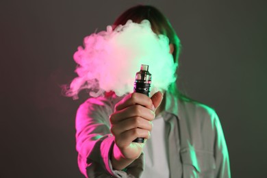 Photo of Woman using electronic smoking device in neon lights on grey background, selective focus