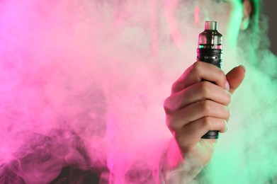 Photo of Woman using electronic smoking device in neon lights on grey background, closeup