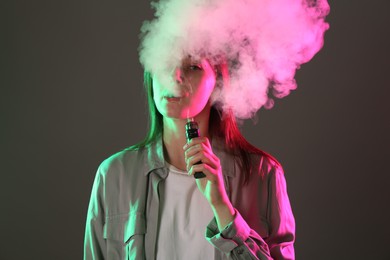 Photo of Woman using electronic smoking device in neon lights on grey background