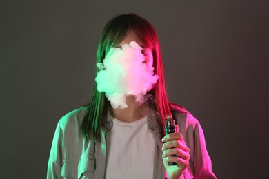 Photo of Woman using electronic smoking device in neon lights on grey background