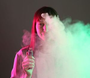 Photo of Woman using electronic smoking device in neon lights on grey background