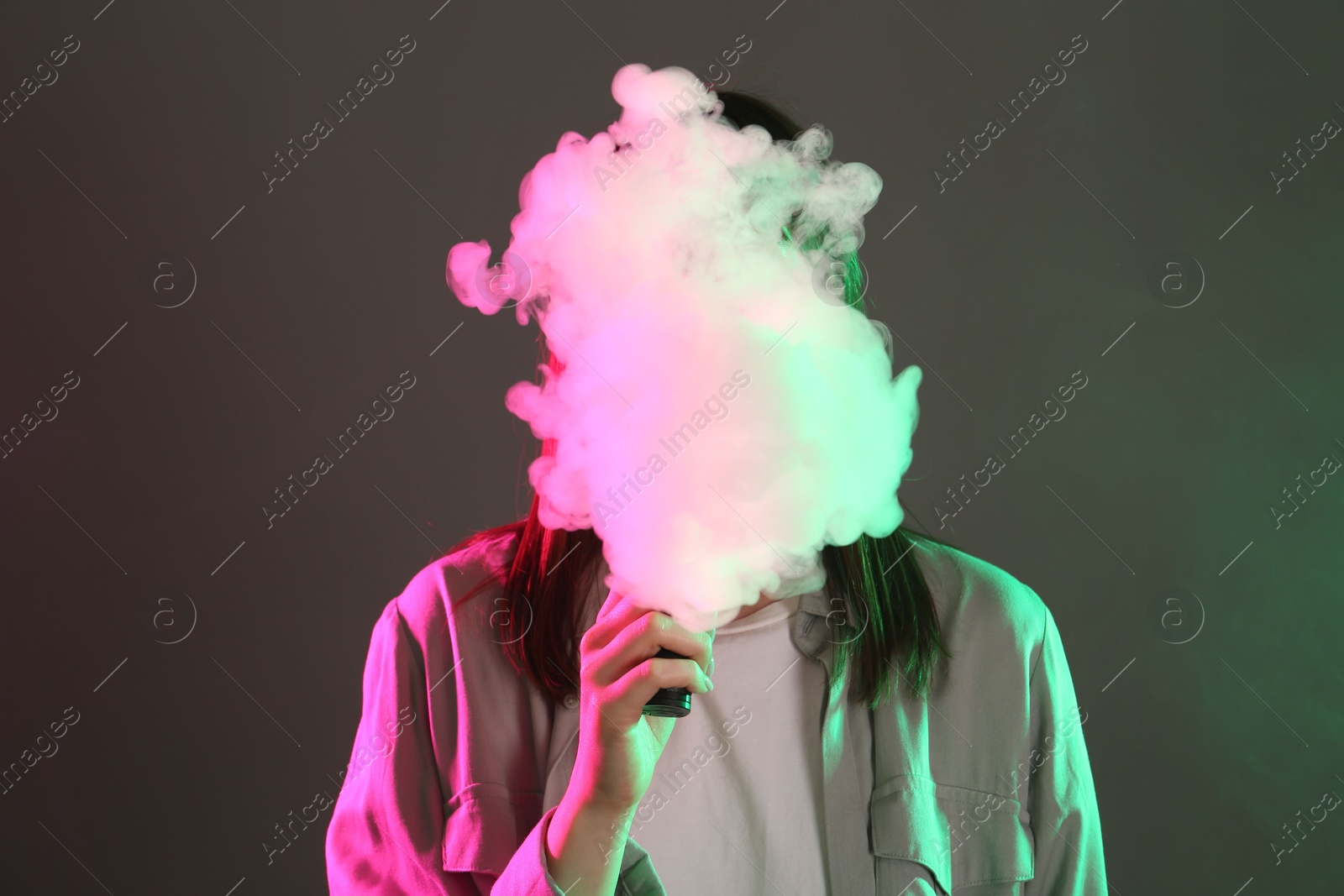 Woman using electronic smoking device in neon lights on grey background Photo of Woman using electronic smoking device in neon lights on grey background