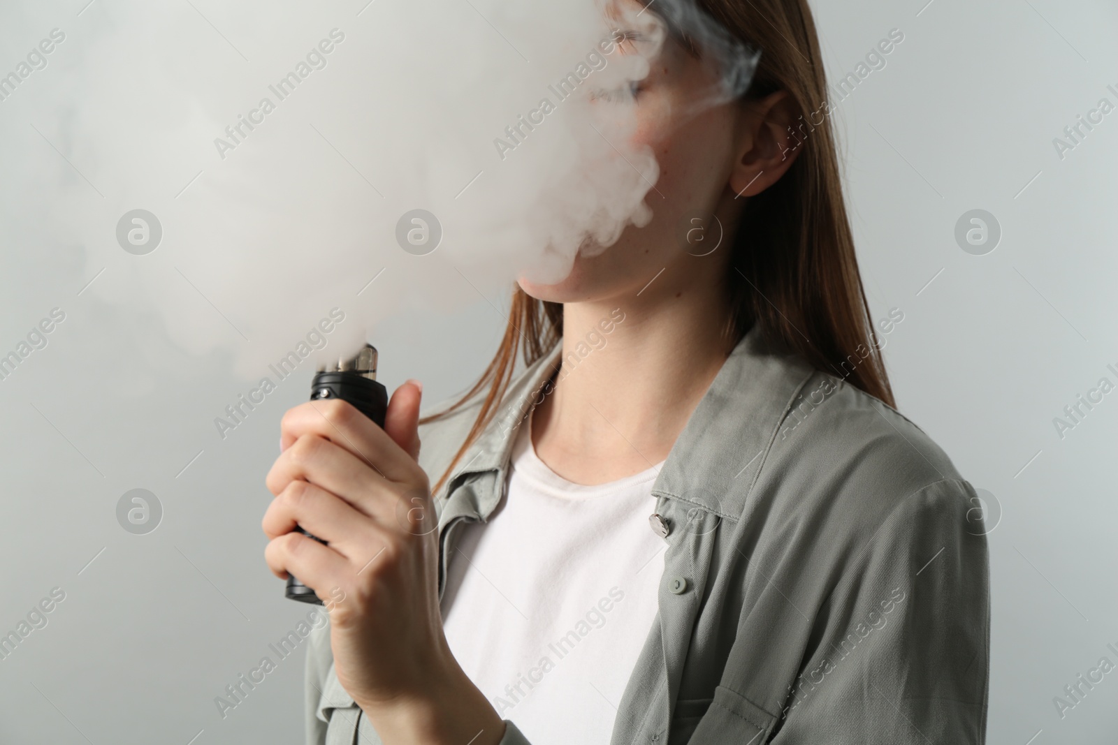 Woman using electronic smoking device on light grey background Photo of Woman using electronic smoking device on light grey background