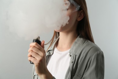 Photo of Woman using electronic smoking device on light grey background