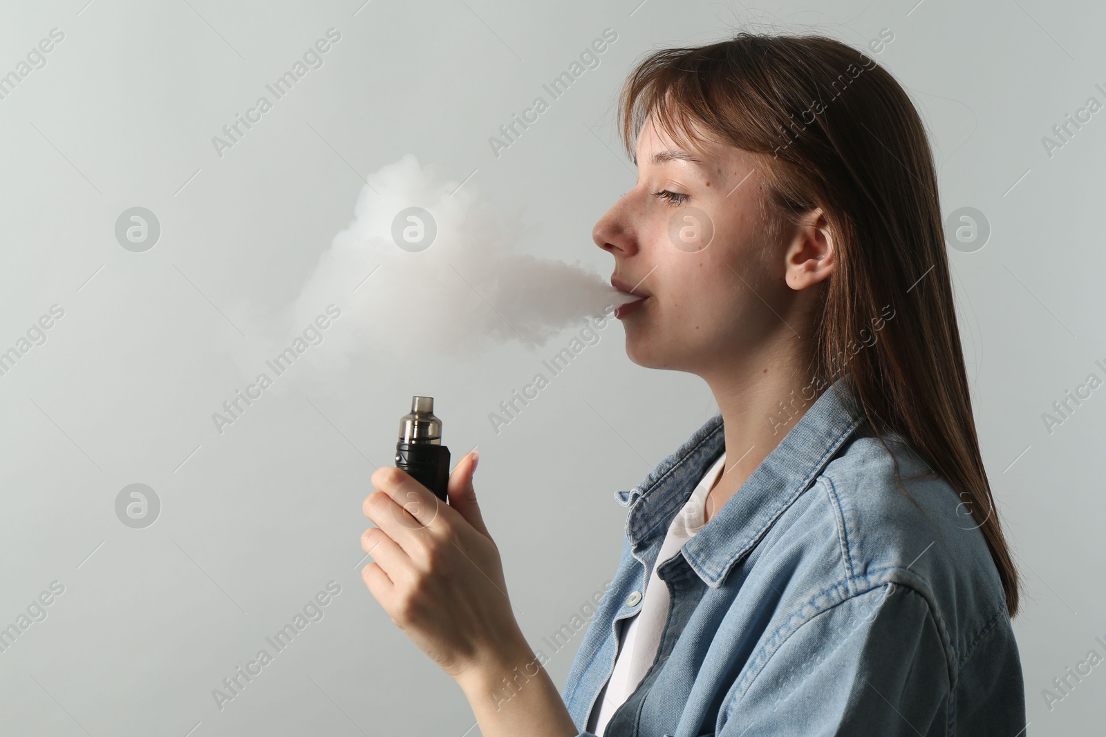 Woman using electronic smoking device on light grey background, space for text Photo of Woman using electronic smoking device on light grey background, space for text