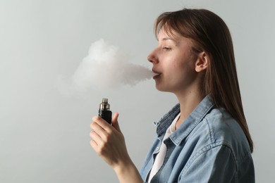 Photo of Woman using electronic smoking device on light grey background, space for text