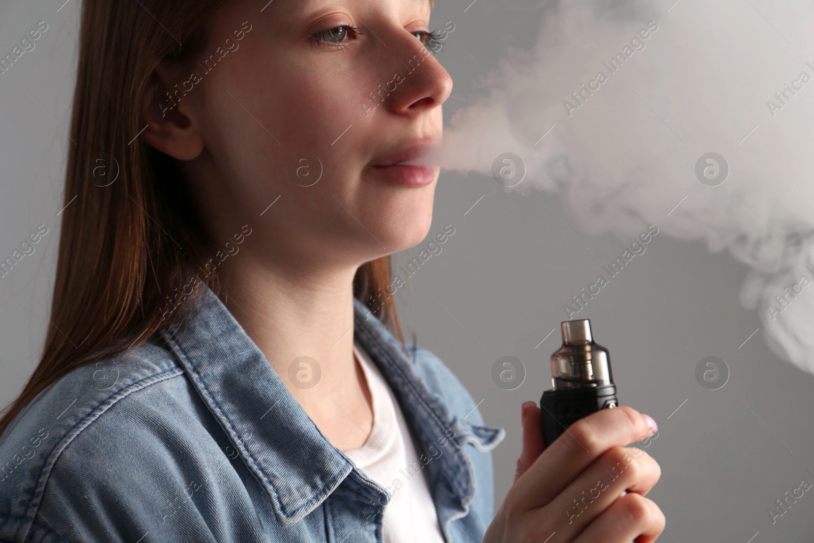 Woman using electronic smoking device on grey background Photo of Woman using electronic smoking device on grey background
