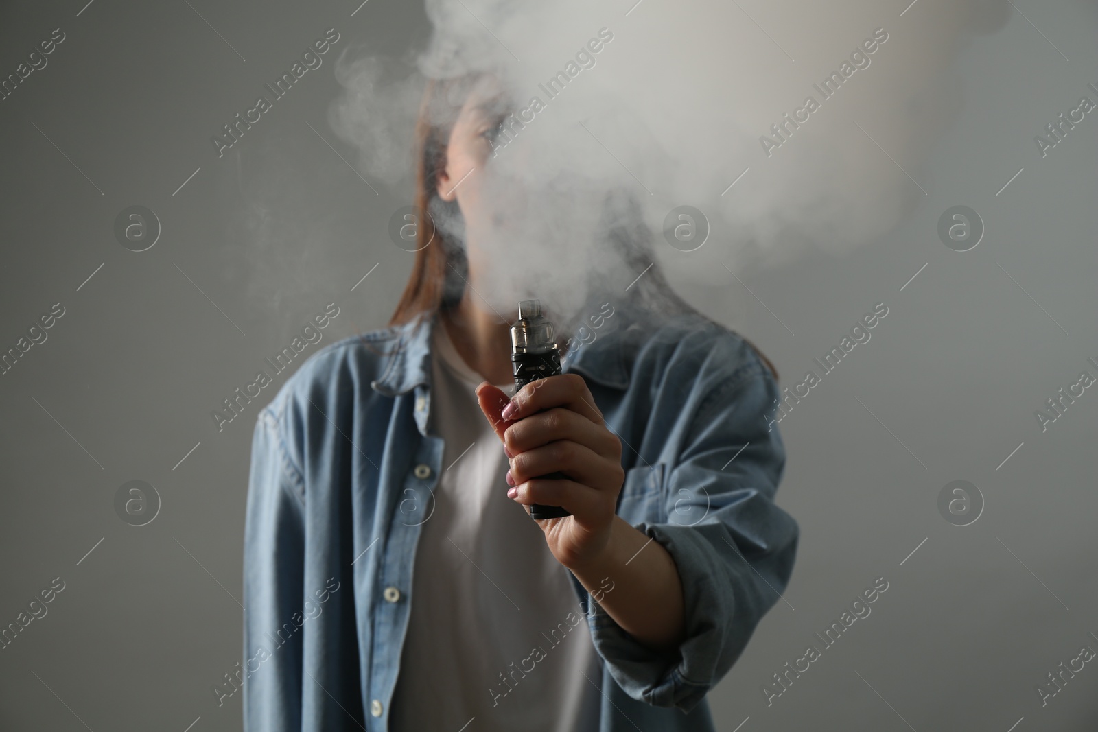 Woman using electronic smoking device on grey background Photo of Woman using electronic smoking device on grey background