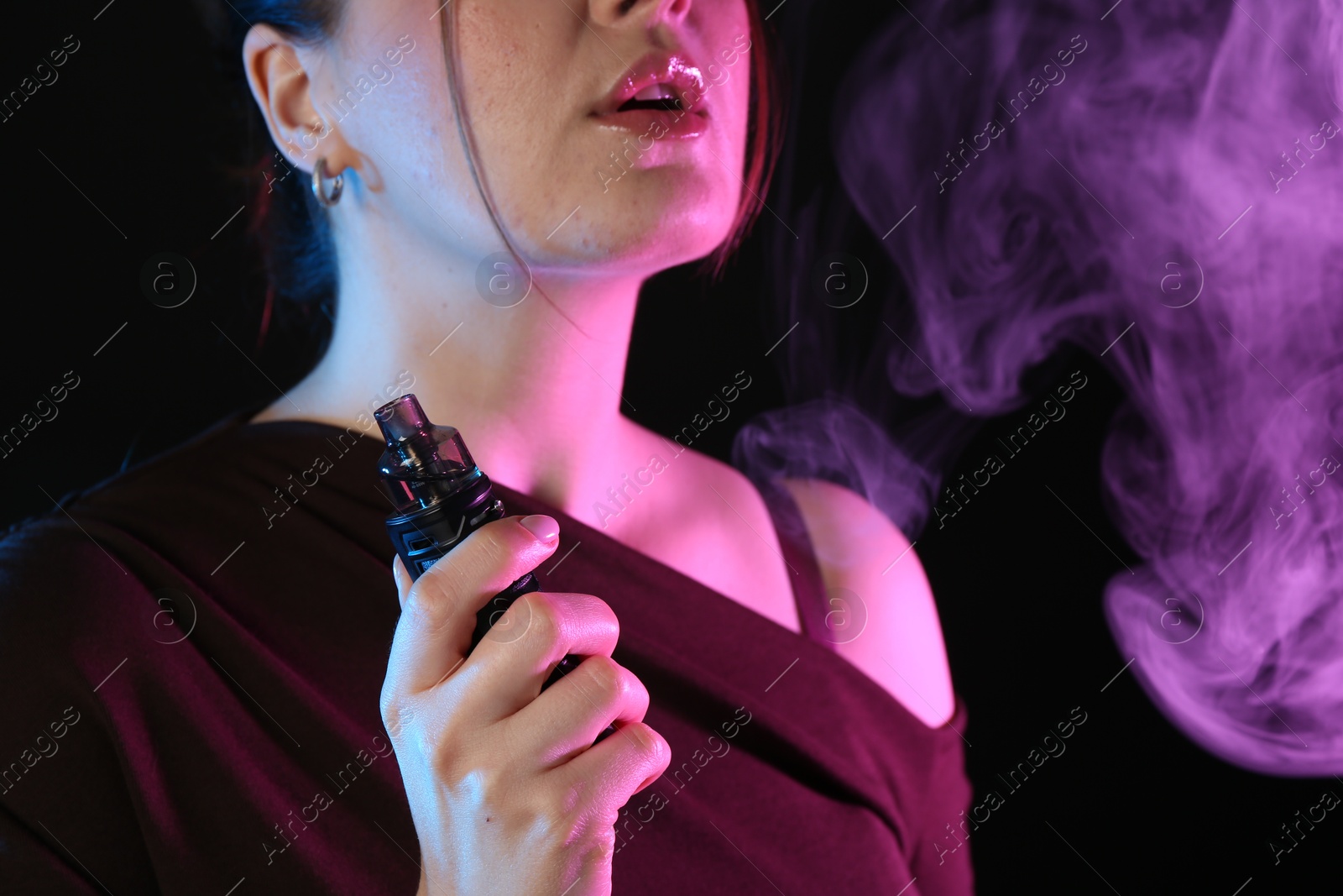 Woman using electronic smoking device in neon lights on black background, closeup Photo of Woman using electronic smoking device in neon lights on black background, closeup