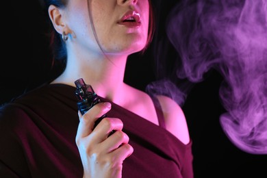 Photo of Woman using electronic smoking device in neon lights on black background, closeup