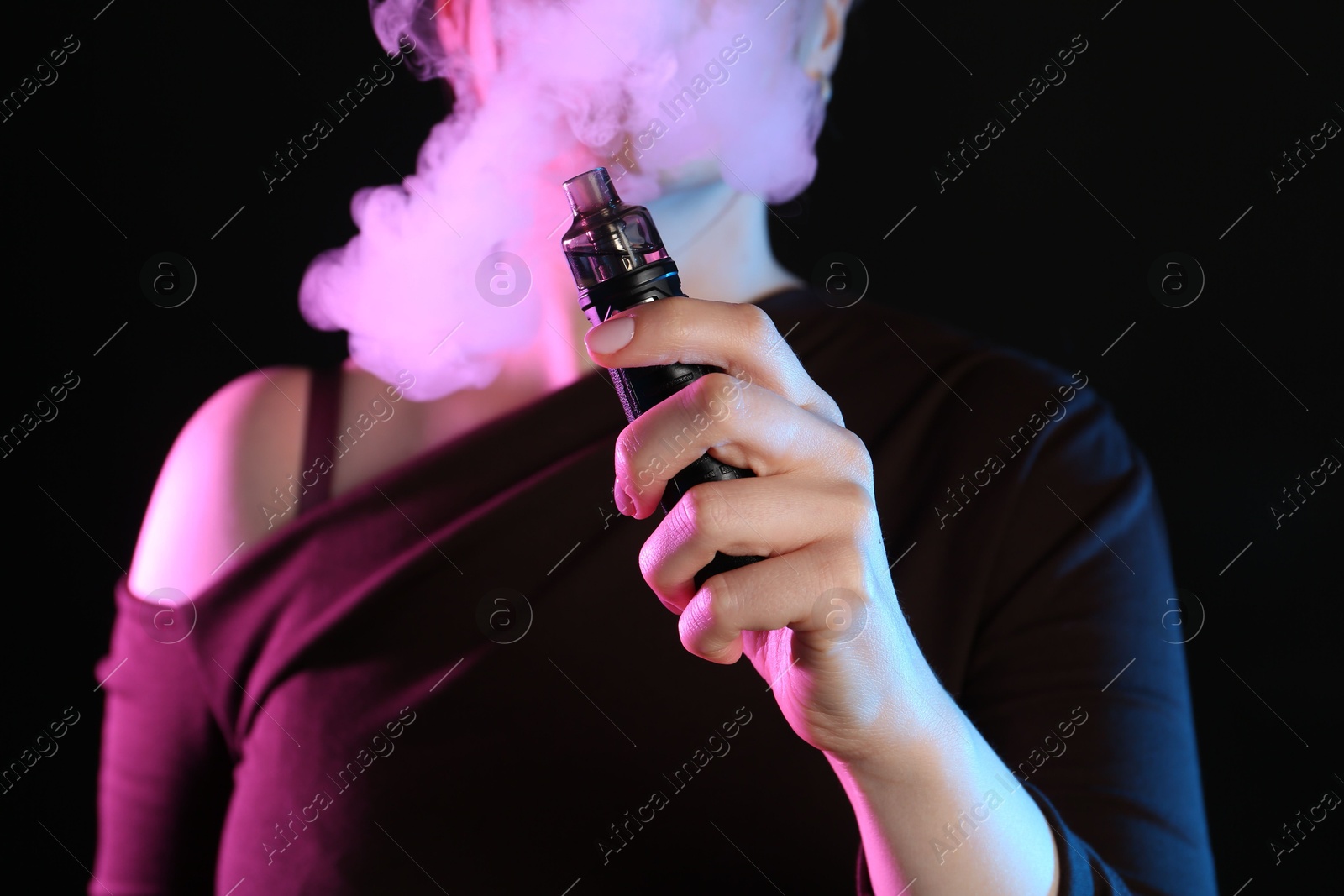 Woman using electronic smoking device in neon lights on black background, closeup Photo of Woman using electronic smoking device in neon lights on black background, closeup