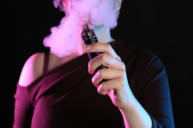 Photo of Woman using electronic smoking device in neon lights on black background, closeup