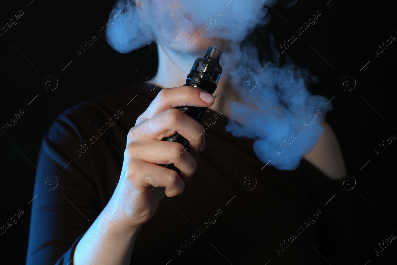 Woman using electronic smoking device in neon lights on black background, closeup Photo of Woman using electronic smoking device in neon lights on black background, closeup