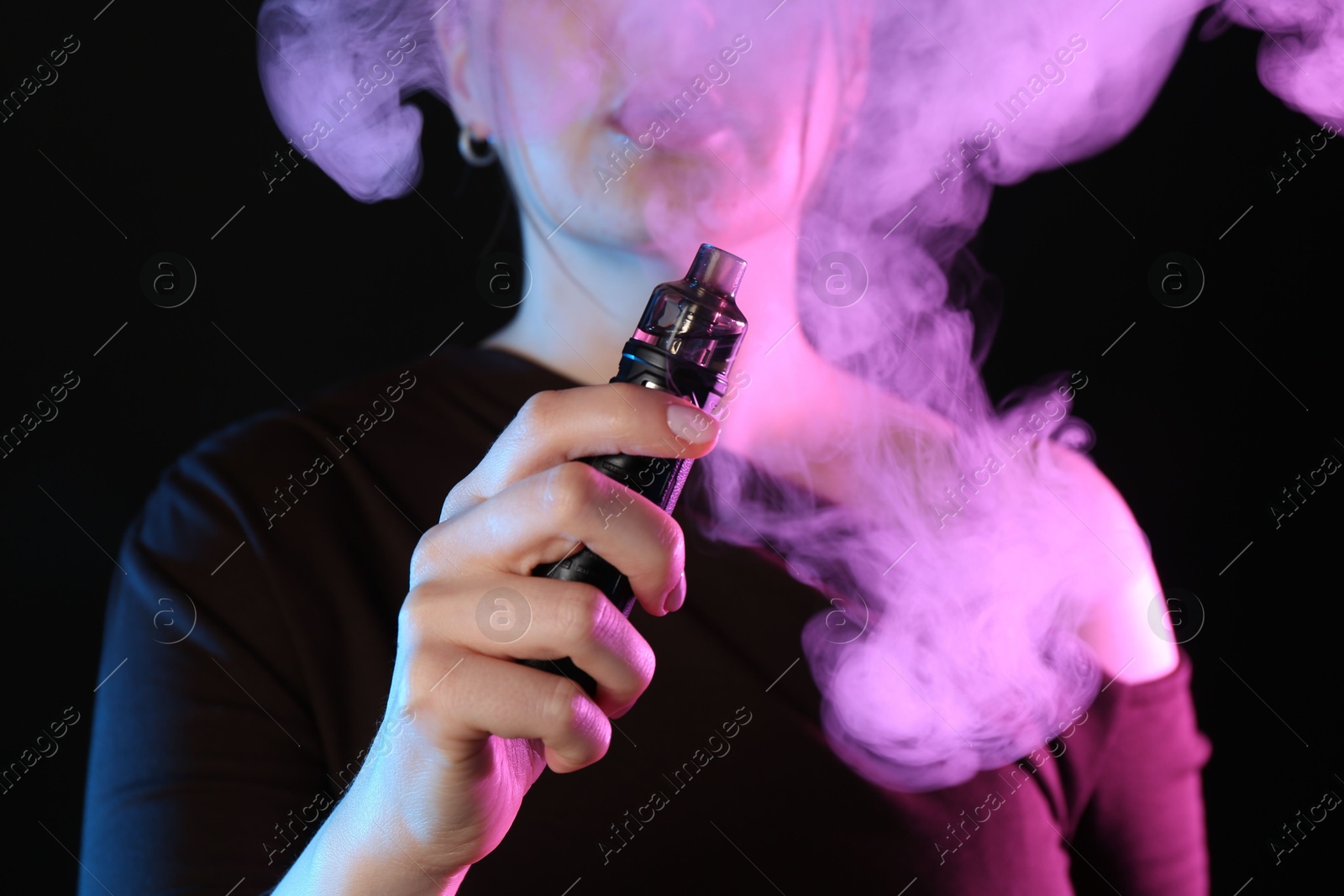 Woman using electronic smoking device in neon lights on black background, closeup Photo of Woman using electronic smoking device in neon lights on black background, closeup