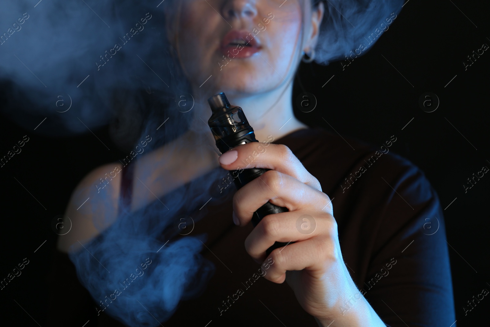 Woman using electronic smoking device in neon lights on black background, closeup Photo of Woman using electronic smoking device in neon lights on black background, closeup