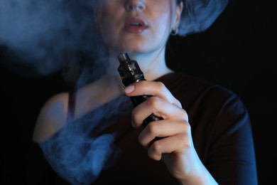 Photo of Woman using electronic smoking device in neon lights on black background, closeup