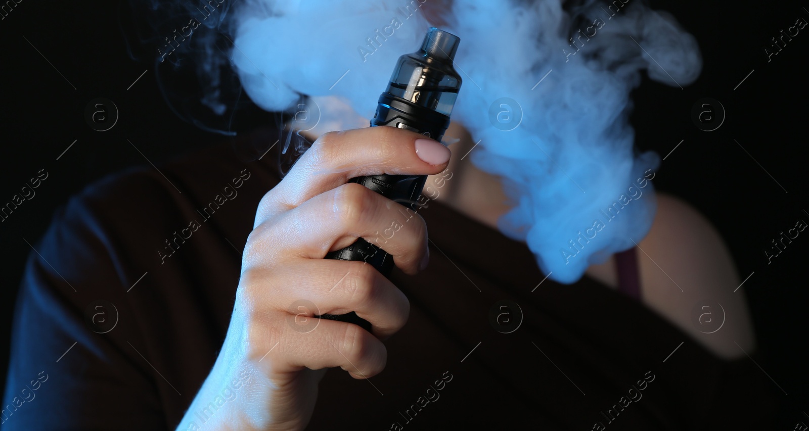 Woman using electronic smoking device in neon lights on black background, closeup Photo of Woman using electronic smoking device in neon lights on black background, closeup