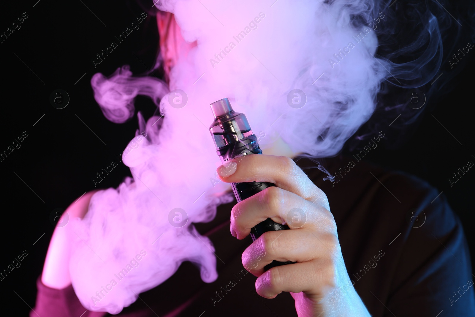 Woman using electronic smoking device in neon lights on black background Photo of Woman using electronic smoking device in neon lights on black background