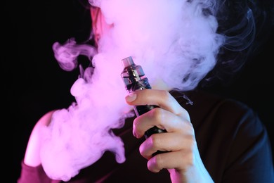 Photo of Woman using electronic smoking device in neon lights on black background