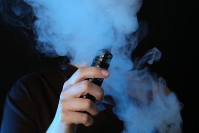 Photo of Woman using electronic smoking device in neon lights on black background