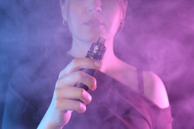 Photo of Woman using electronic smoking device in neon lights on dark background, closeup
